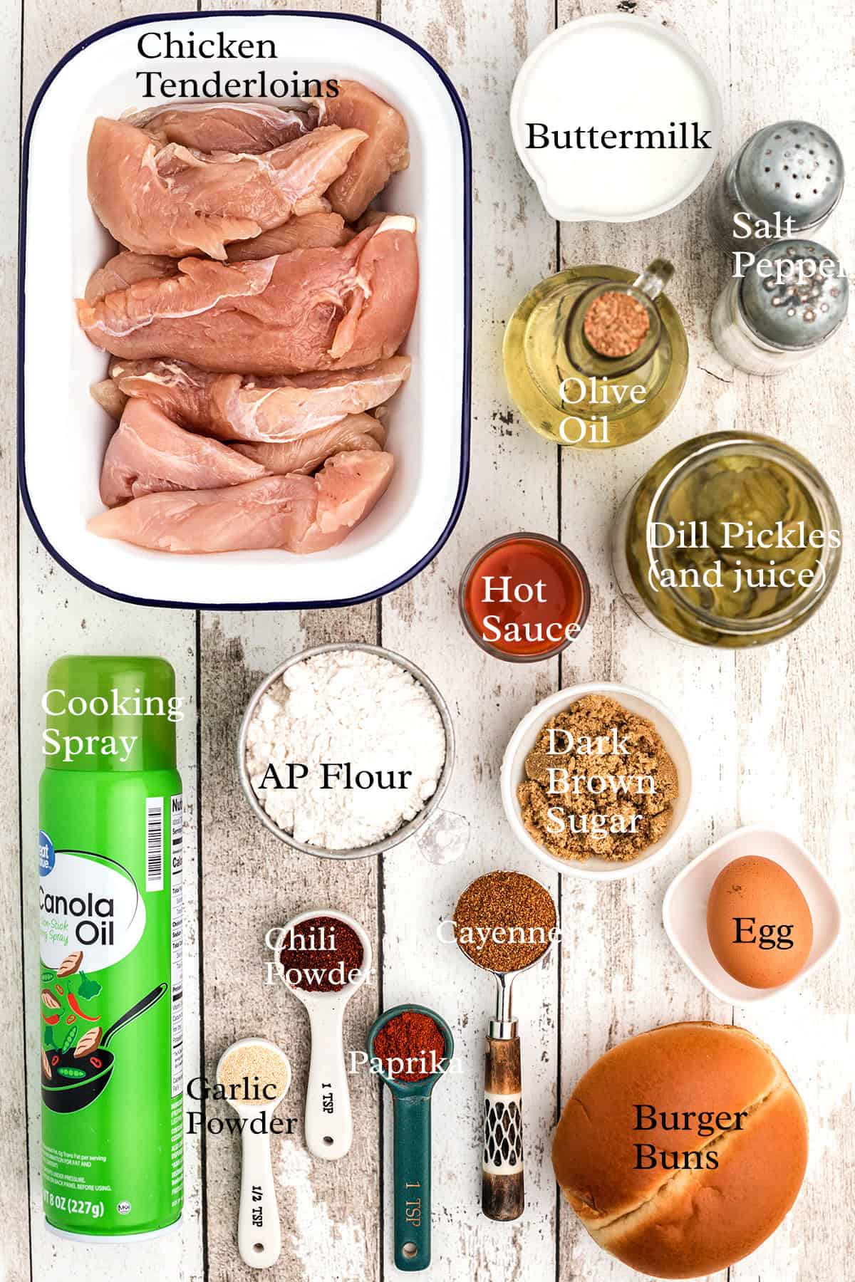 Ingredients for a chicken sandwich laid out, including raw chicken, flour, spices, oil, egg, and buns.