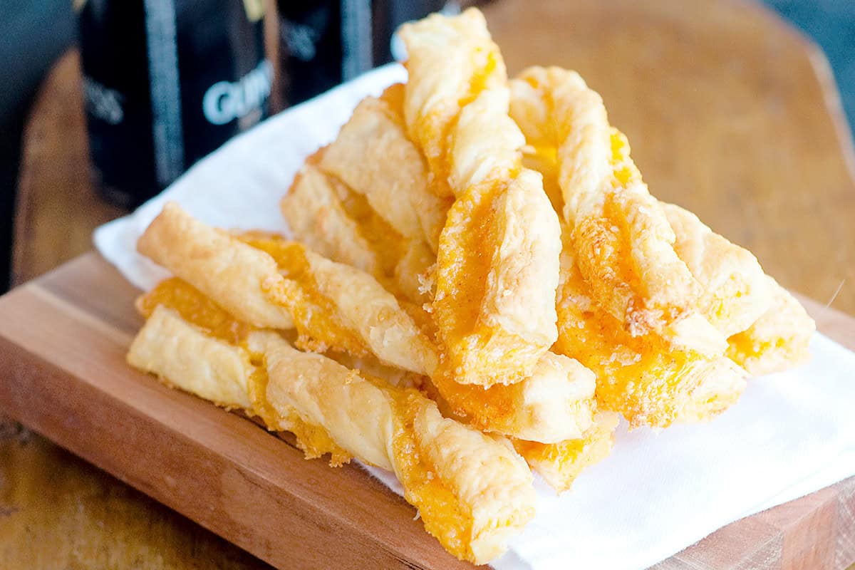 A mound of cheese straws on a wooden board.