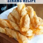 A stack of golden, twisted puff pastry cheese straws on a wooden board with a napkin.