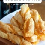 Golden puff pastry cheese straws stacked on a wooden board, with text label and website name above.