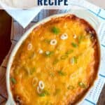Oval dish of cheesy refried bean dip topped with green onions, next to a basket of tortilla chips.
