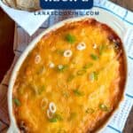 Baked refried bean dip topped with melted cheese and sliced green onions in a casserole dish.