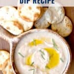 Bowl of white bean dip with olive oil and herbs, surrounded by round crackers on a wooden table.