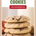 A stack of cowboy cookies with chocolate chips and pecans, with a glass of milk in the background.