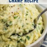 A bowl of creamy Irish champ mashed potatoes with chopped green onions and pepper, with a spoon in it.