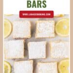 Overhead view of powdered sugar-covered lemon bars arranged with lemon slices on a light surface.