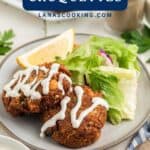 A plate with two salmon croquettes, salad, a lemon wedge, and a drizzle of white sauce.