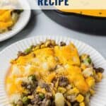 A serving of shepherd’s pie with beef, vegetables, and melted cheese on a white plate next to a baking dish.