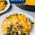 A plate of shepherd’s pie with ground meat, peas, corn, and melted cheese, with more pie in the background.