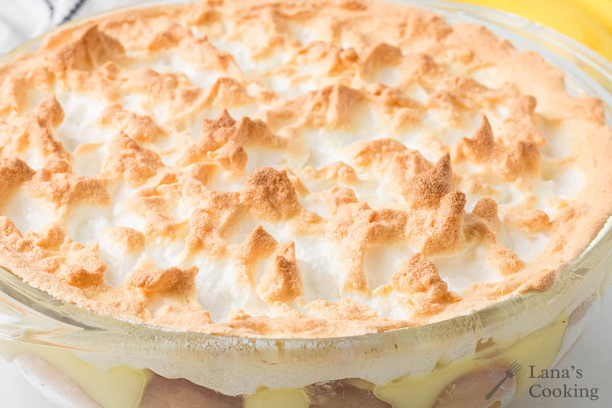 A close-up of a banana pudding with meringue in a clear dish, with golden peaks on top.