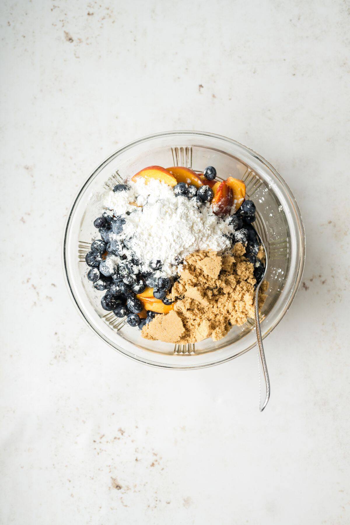 Sliced peaches and blueberries in a bowl with melted butter, cornstarch, and brown sugar.
