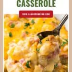 Close-up of cheesy ham and potato casserole on a spoon, topped with melted cheese and chopped herbs.