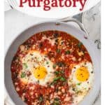 Frying pan with eggs poached in tomato sauce, garnished with herbs and cheese. Text: Eggs in Purgatory.