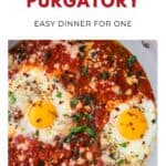 Two eggs cooked in a spicy tomato sauce, garnished with herbs in a skillet. Text: Eggs in Purgatory.