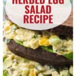 Close-up of a herbed egg salad sandwich on dark bread with text overlay: Herbed Egg Salad Recipe.
