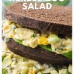 Close-up of a herbed egg salad sandwich on dark bread with lettuce, shown with text overlay and website link.