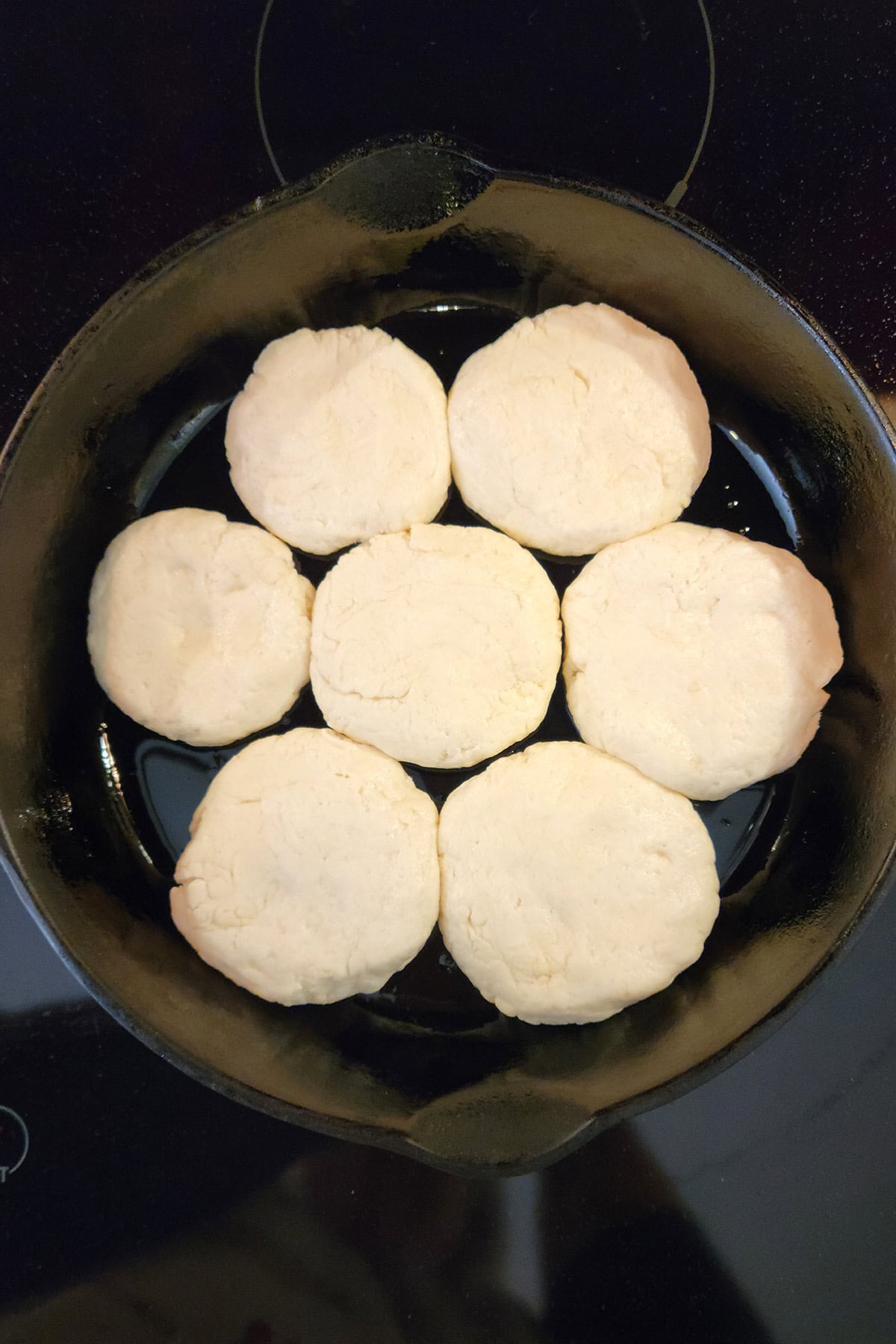 Seven unbaked biscuits arranged in a cast iron skillet, ready to be baked.