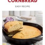 A slice of golden cornbread being lifted from a cast iron skillet on a kitchen counter.