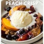 Bowl of blueberry peach crisp topped with a scoop of vanilla ice cream, melting over the warm dessert.