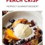 Bowl of blueberry peach crisp topped with a scoop of vanilla ice cream, surrounded by fruit and oat crumble.