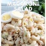 Bowl of creamy macaroni salad topped with sliced boiled eggs, with parsley in the background.