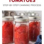 Three jars of home-canned tomatoes sit on a white surface with a blue towel nearby.