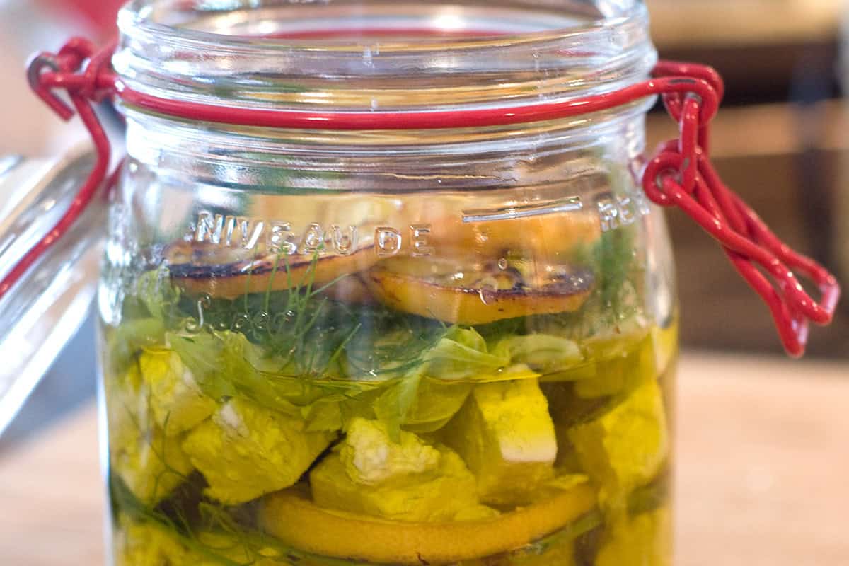 A wire bail jar filled with roasted lemons, dill, feta cheese, and olive oil.