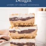 Stack of three peanut butter dessert bars topped with whipped cream and crushed nuts.