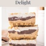 Three stacked peanut butter delight dessert bars topped with whipped cream and crushed nuts.