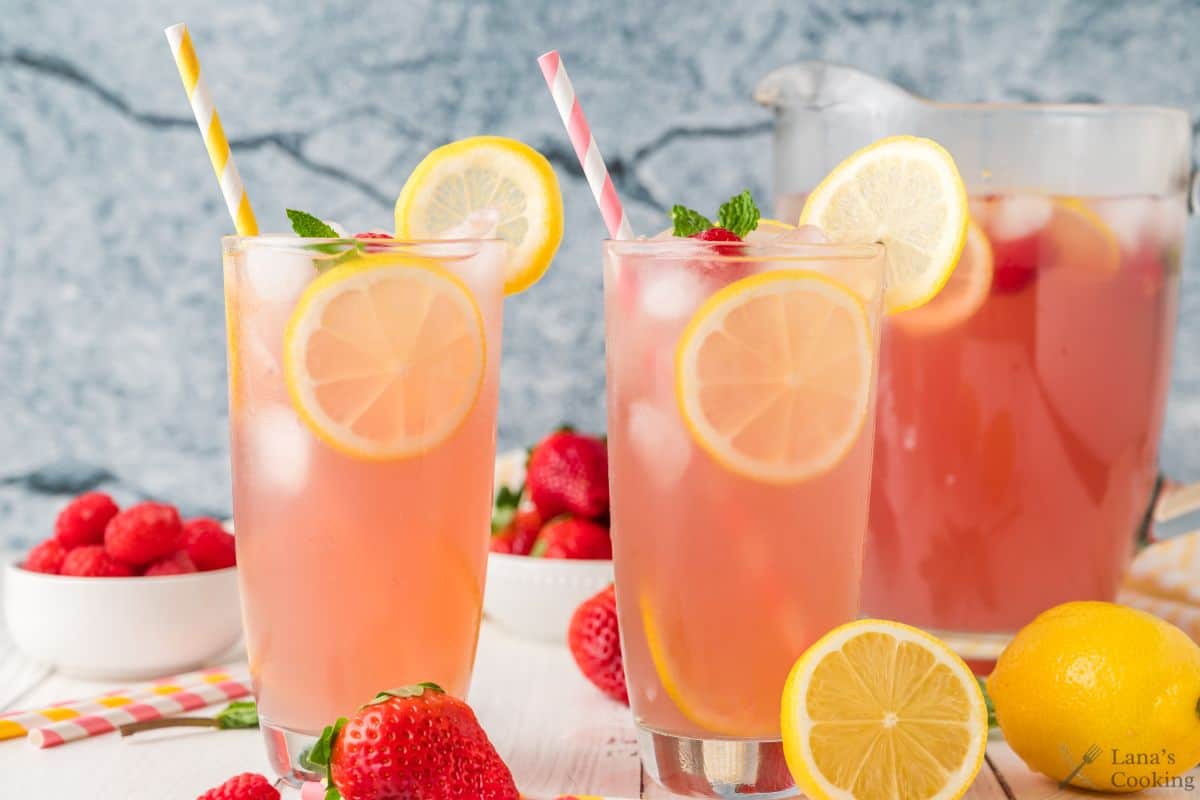 Pink lemonade in tall glasses with slices of lemon and strawberries.