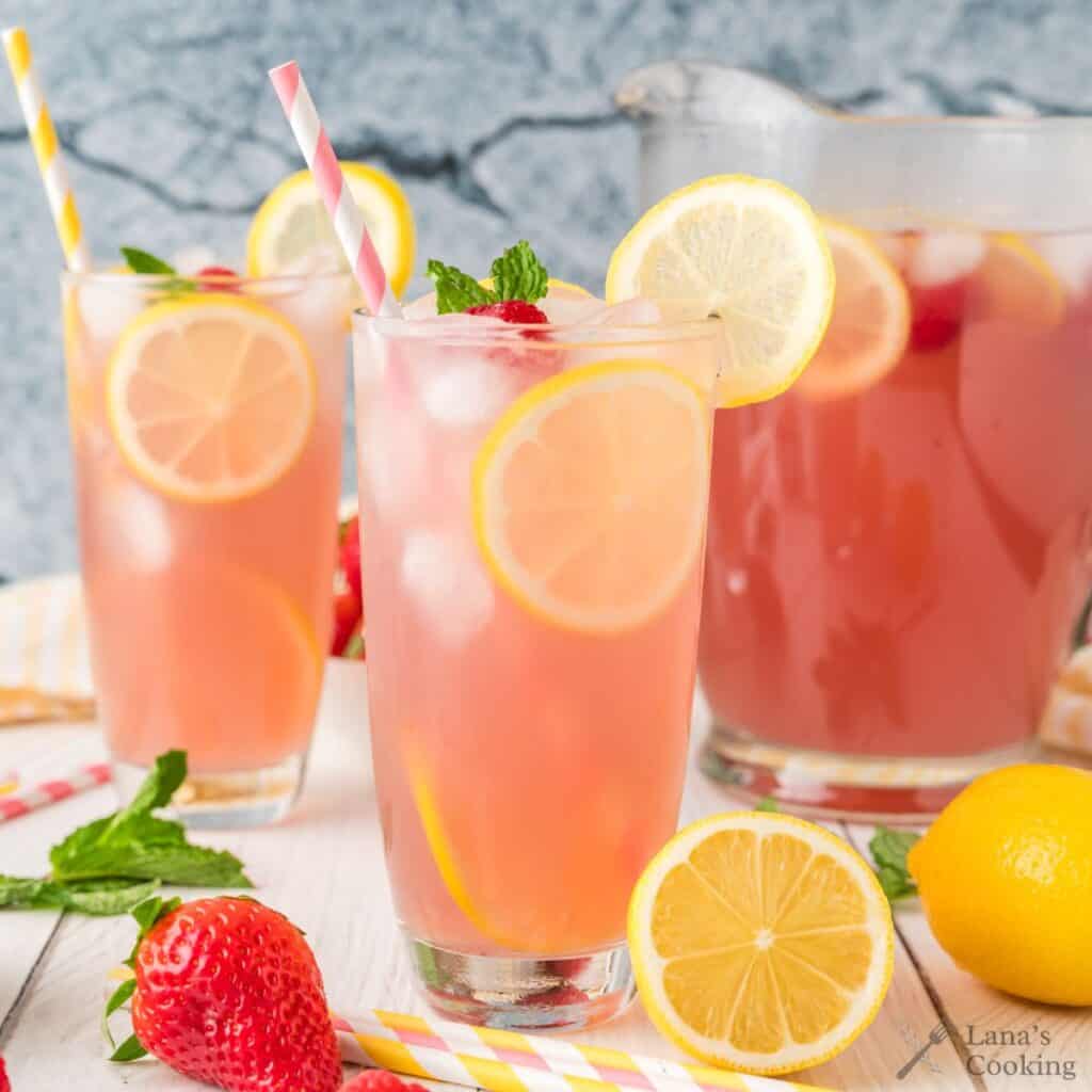 Pink lemonade in tall glasses with slices of lemon and strawberries.