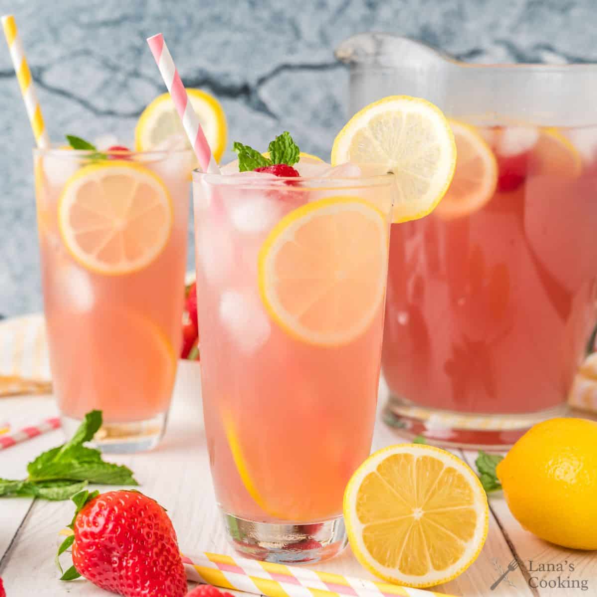 Pink lemonade in tall glasses with slices of lemon and strawberries.