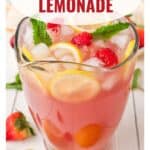 A pitcher of pink lemonade with ice, lemon slices, raspberries, and mint, surrounded by strawberries.