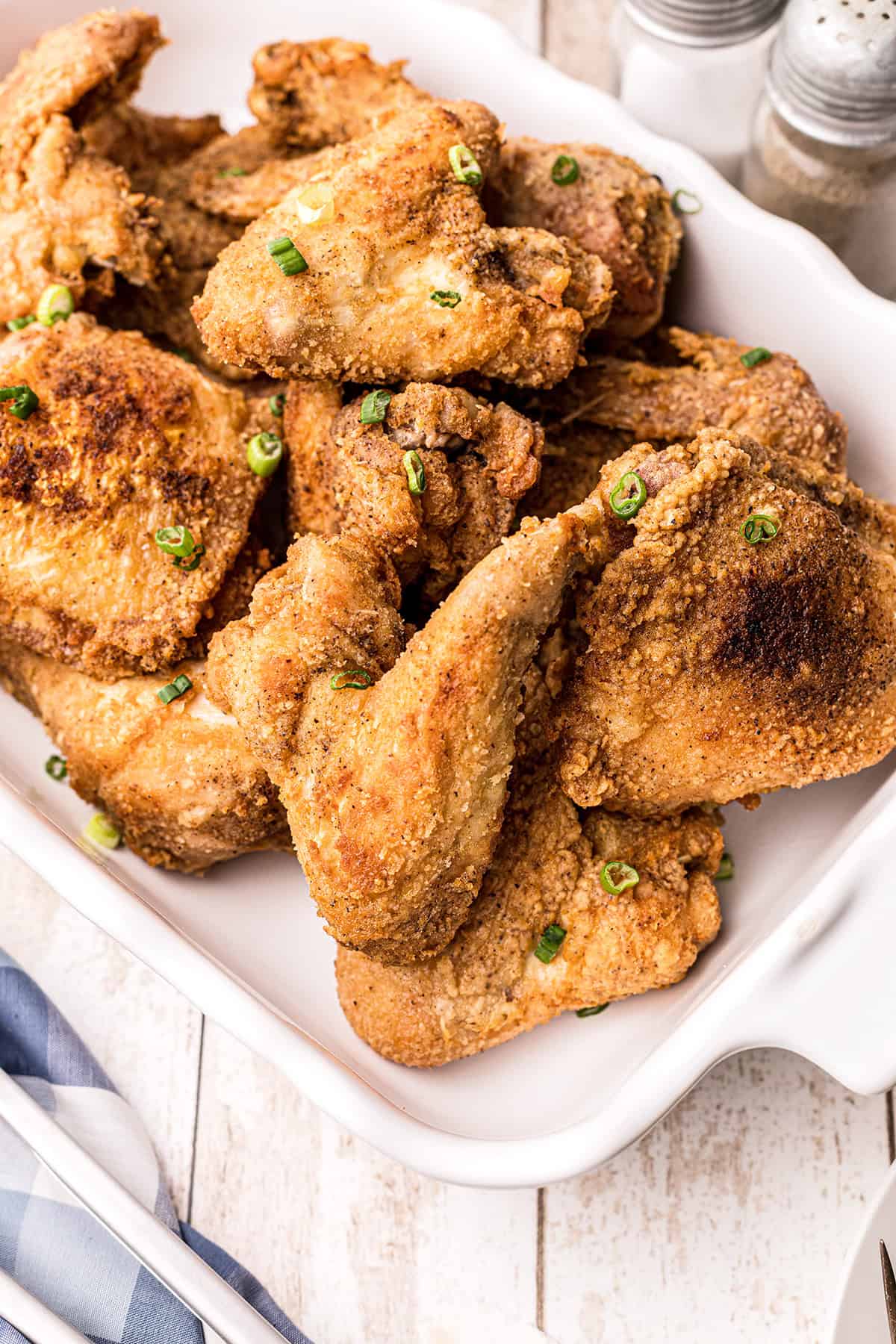 A white dish filled with crispy fried chicken pieces, garnished with chopped green onions.