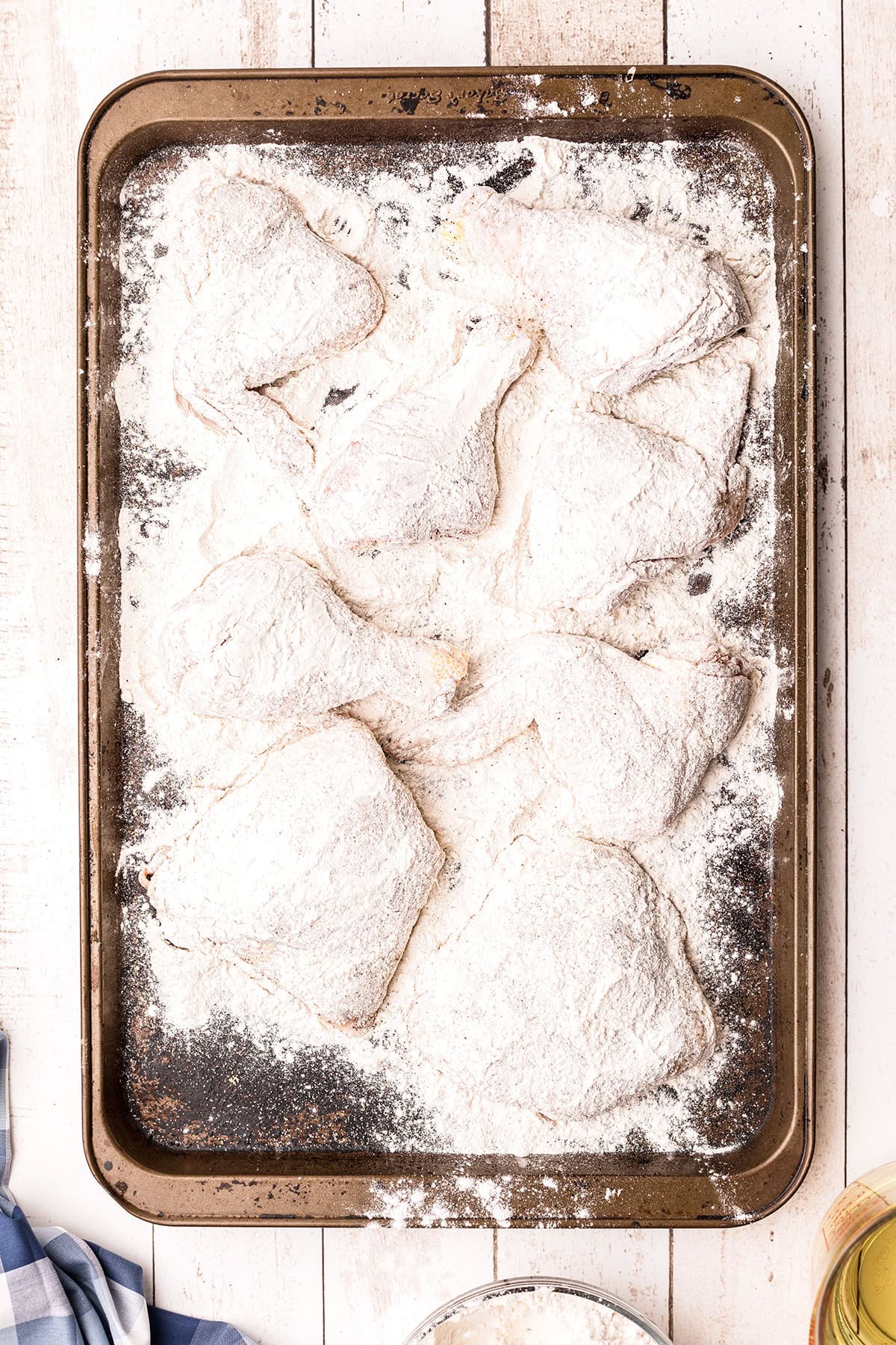 Chicken pieces coated in flour are arranged on a baking sheet, ready to be cooked.