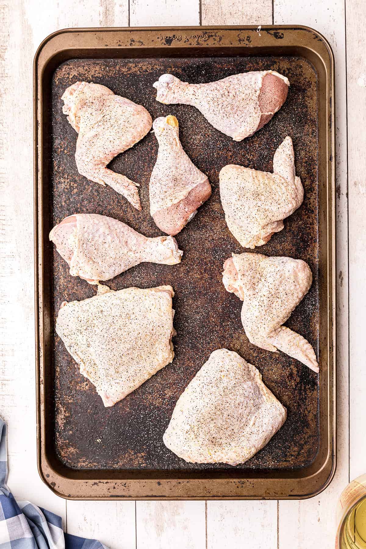 Raw chicken pieces seasoned with pepper arranged on a baking sheet, ready for cooking.
