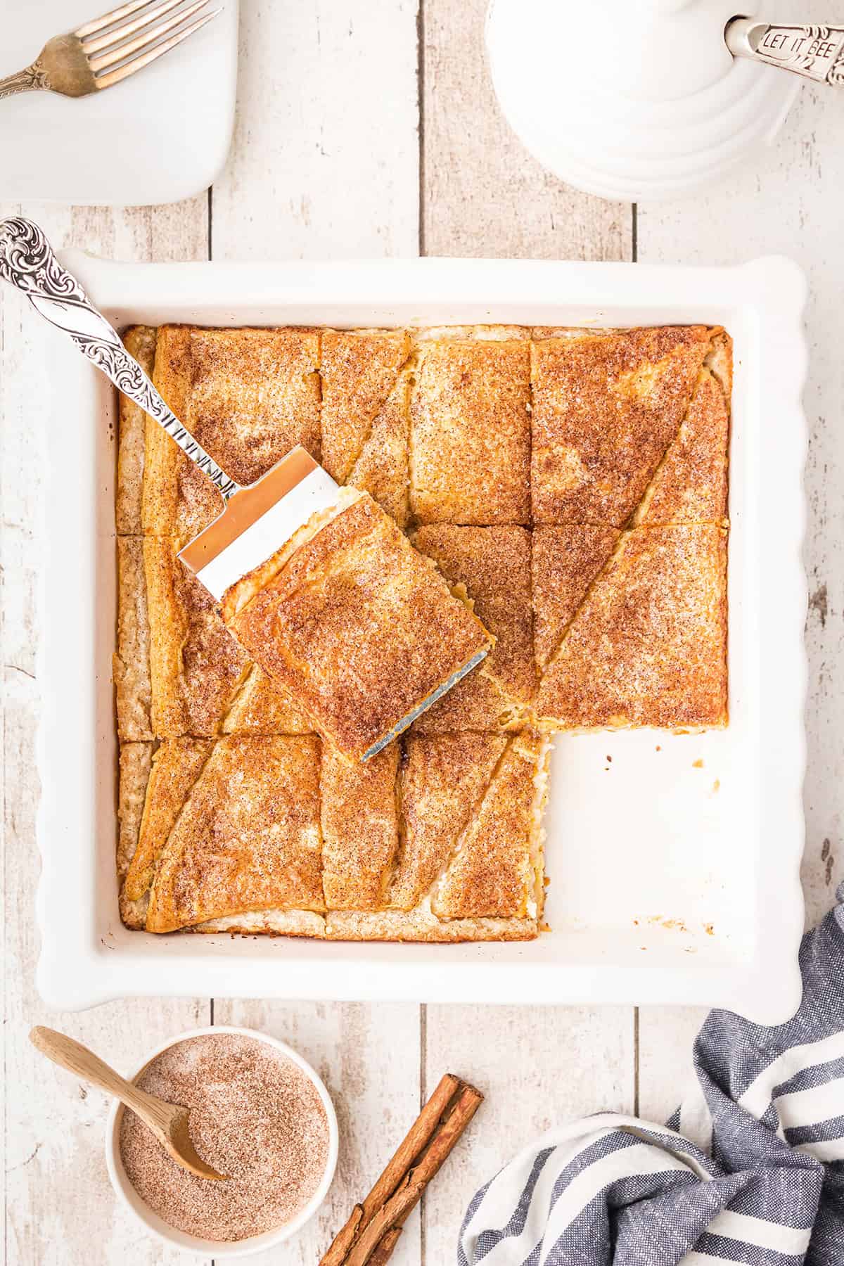 A cinnamon sugar pastry dessert in a white baking dish, with one piece being served.