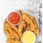 Plate of fried chicken fingers with red and yellow dipping sauces, next to a black and white checkered napkin.