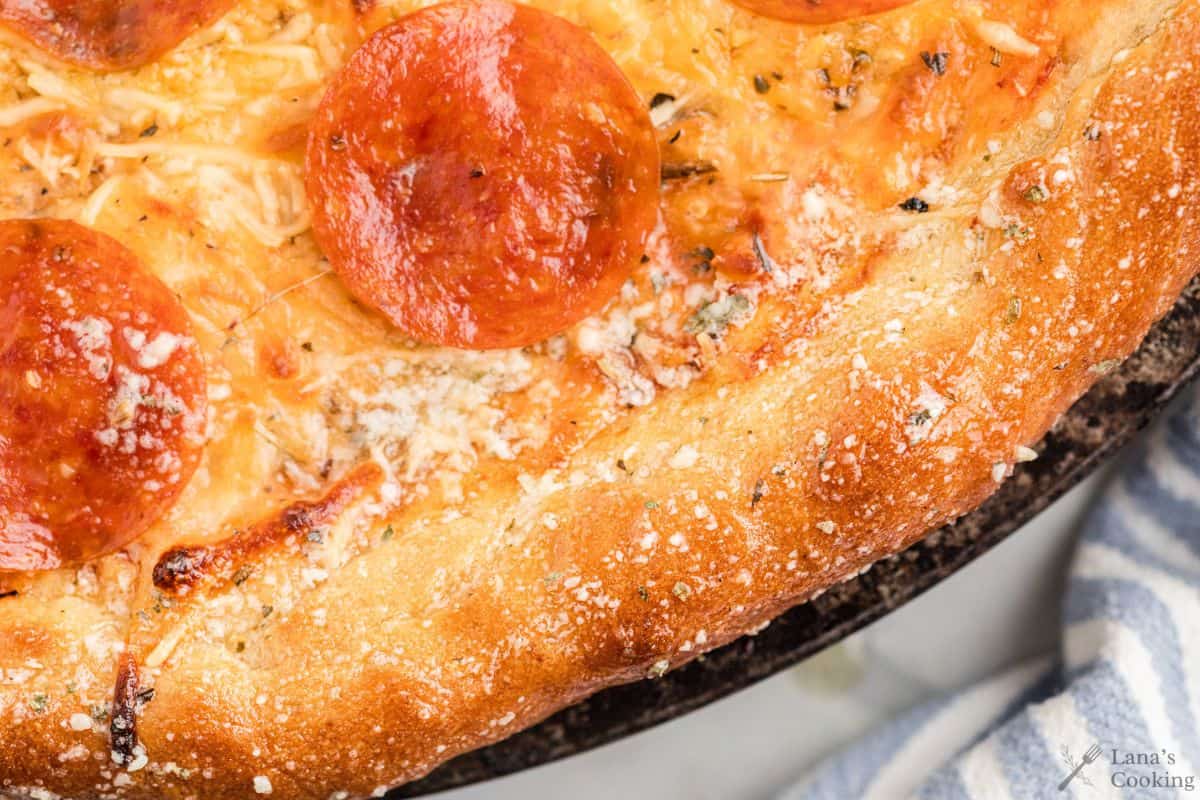 Close-up of a pepperoni pizza with melted cheese, browned crust, and a sprinkle of grated parmesan on the edge.