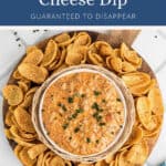 Bowl of sausage cheese dip garnished with chives, surrounded by corn chips on a wooden serving board.