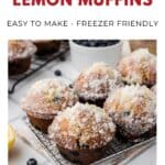 Four sugar-topped blueberry lemon muffins on a cooling rack with blueberries and a lemon slice nearby.