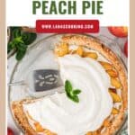 A peach pie topped with whipped cream, missing a slice, with fresh peaches and mint garnish.