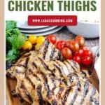 Grilled chicken thighs on a wooden board with cherry tomatoes and parsley in the background.