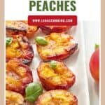 Grilled peach halves garnished with basil leaves on a white platter, with a whole peach nearby.