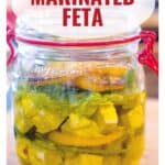 A glass jar of marinated feta with herbs and oil, labeled Marinated Feta and website www.lanascooking.com.