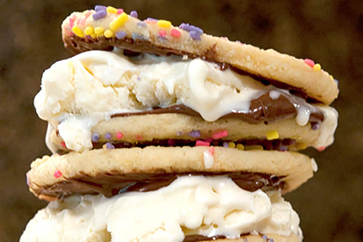 A close-up of stacked ice cream sandwiches made with sugar cookies, nutella spread, vanilla ice cream, and colorful sprinkles.