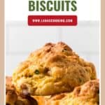 Golden brown bacon cheddar biscuits stacked on a light surface, with text promoting a recipe from lanascooking.com.