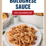 Plate of spaghetti with Bolognese sauce, topped with herbs and cheese, with text Traditional Bolognese Sauce.