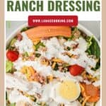A salad topped with buttermilk ranch dressing, shredded cheese, egg, tomatoes, carrots, and bacon.