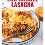 A plate of egg noodle lasagna with melted cheese, ground meat, and a slice of garlic bread on the side.